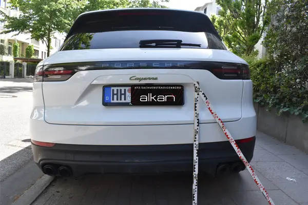 Das Bild zeigt das Heck eines weißen Porsche Cayenne mit Messlatte zur Schadensdokumentation.