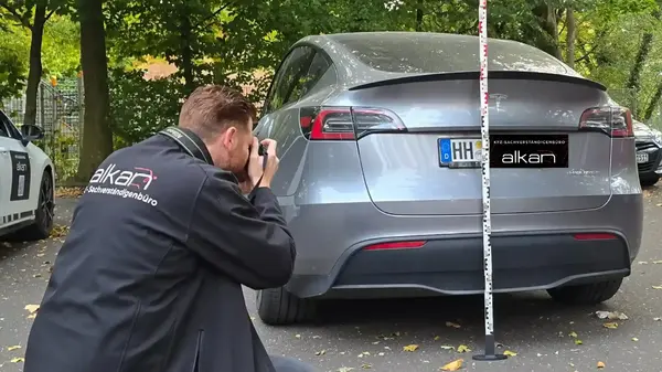 KFZ-Gutachter fotografiert ein beschädigtes Auto mit Messstab für Schadensdokumentation.