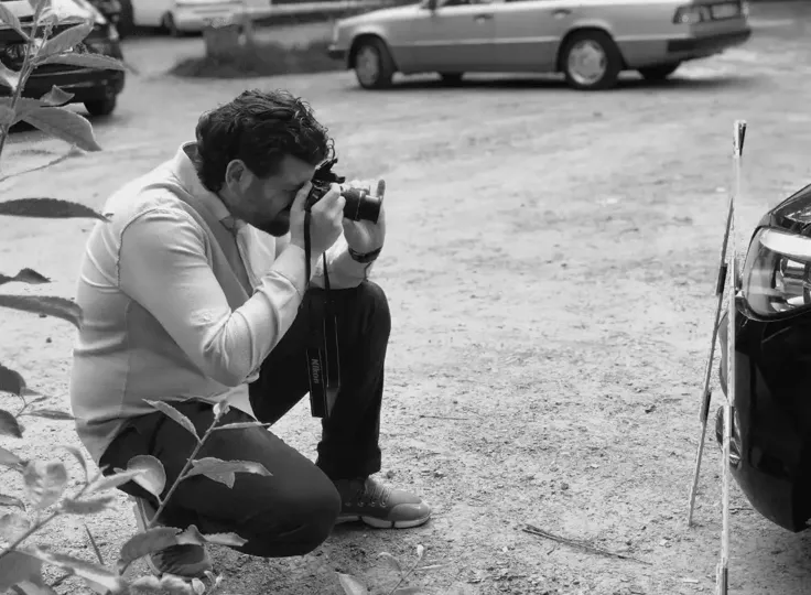 Ein Fotograf kniet auf einem Parkplatz und fotografiert ein Auto aus nächster Nähe.